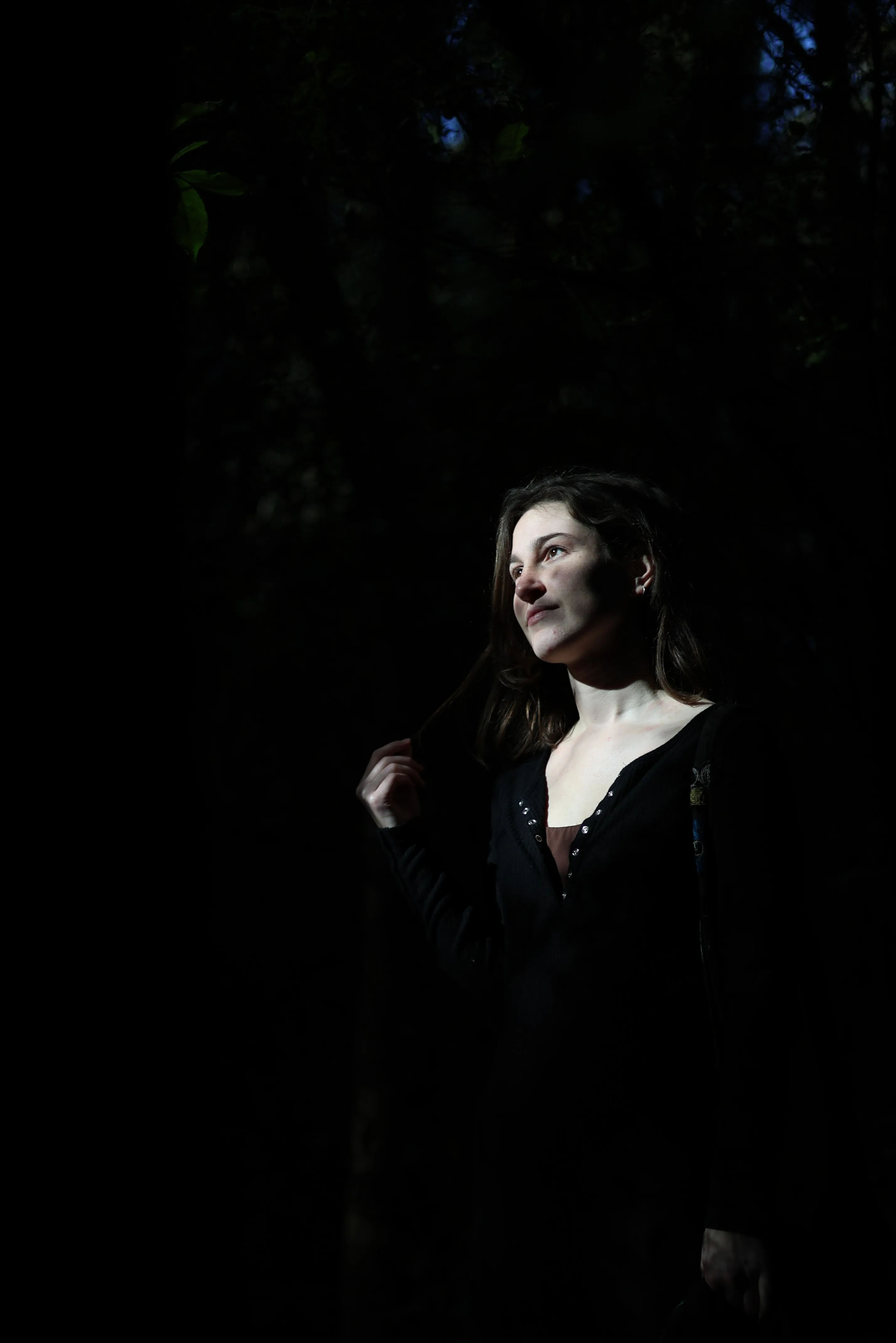 A narrow shaft of forest sunlight illuminates Norma’s face against the surrounding shadows