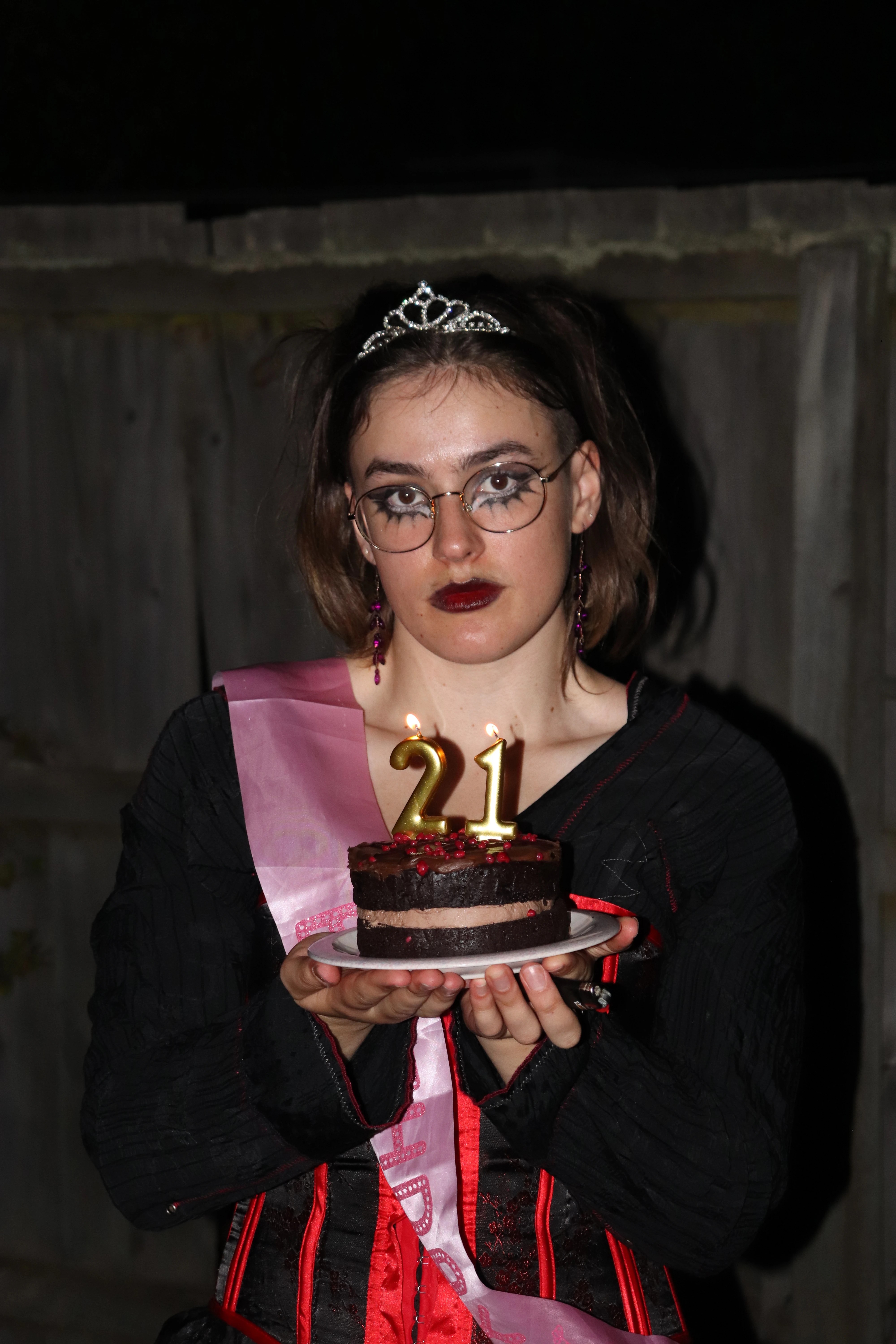 Ella wears a tiara and a 21 sash while holding a small birthday cake with lit candles